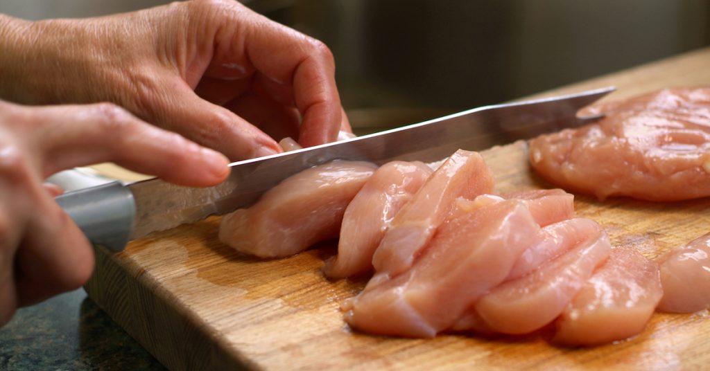 Picture of a Woman Cutting Raw Chicken on a Wooden Cutting Board