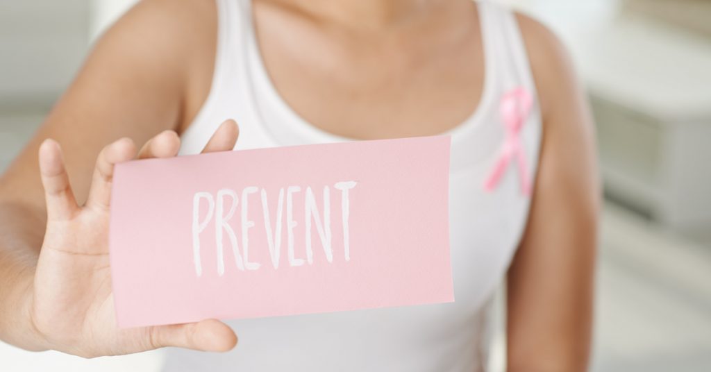 Woman in white tank top holds up "prevent" sign in reference to breast cancer
