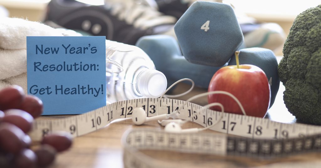 Picture of weights, healthy food, and a measuring tape on a table.