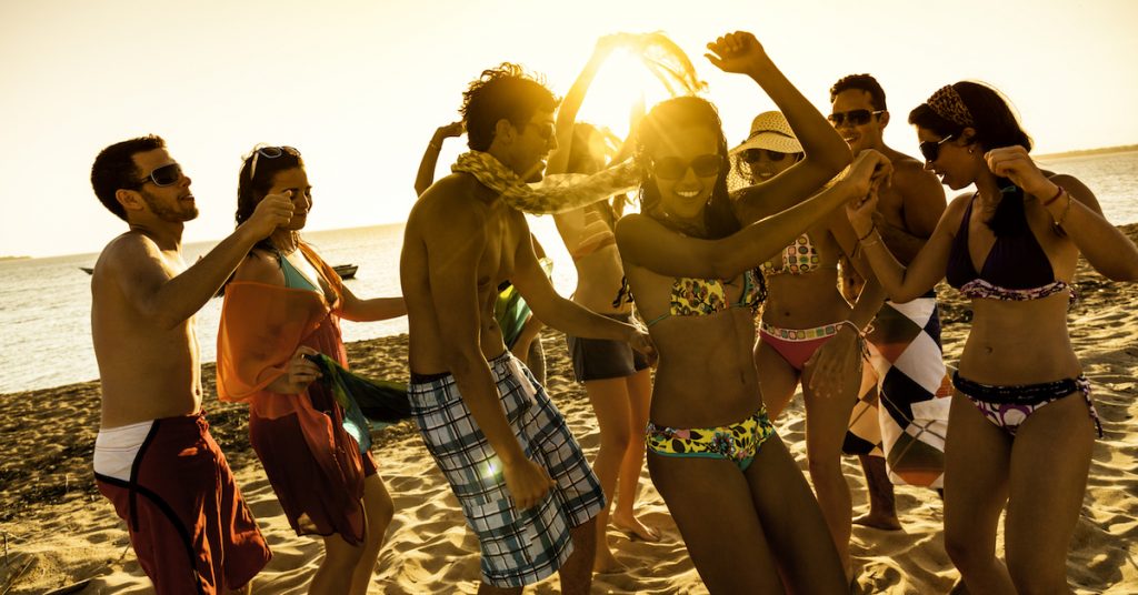 Spring break backlit group of young people dancing on beach